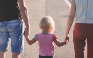 Parents hold the hands of their young daughter while walking down the street