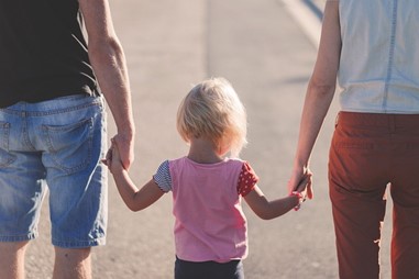 Parents hold the hands of their young daughter while walking down the street