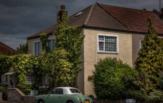 A vibrant traditional British cottage with a turquoise classic car parked out front