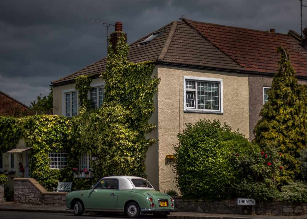 A vibrant traditional British cottage with a turquoise classic car parked out front