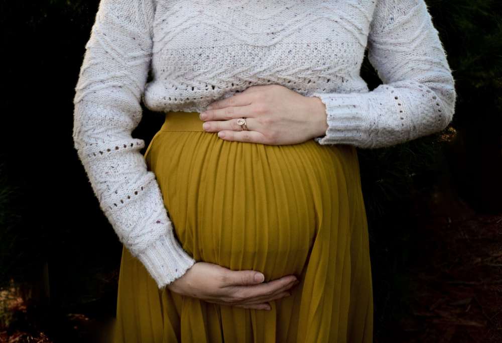 A image of a woman holding her pregnant belly against a black background