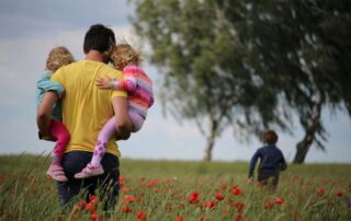 A father carries his children while walking through a poppy field on a sunny day