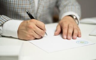 A closeup image of a man signing his will at a desk