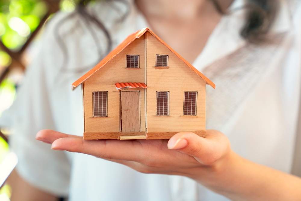 a woman holding a small wooden house in her hand