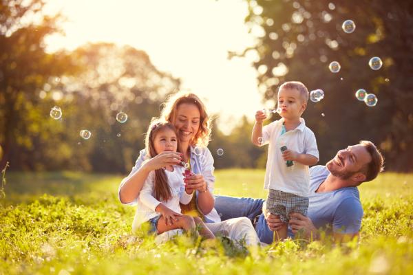 A happy young couple and their children relax and blow bubbles in a field on a sunny day.