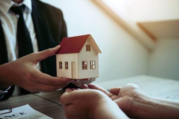 Businessmen exchange a small wooden model of a house