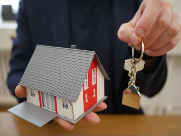 A man holds a plastic model of a house and a set of house keys