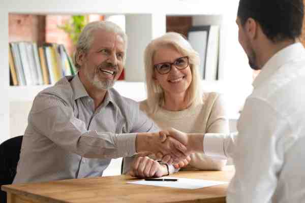 A cheerful elderly couple shake the hand of a Probate solicitor during a consultation