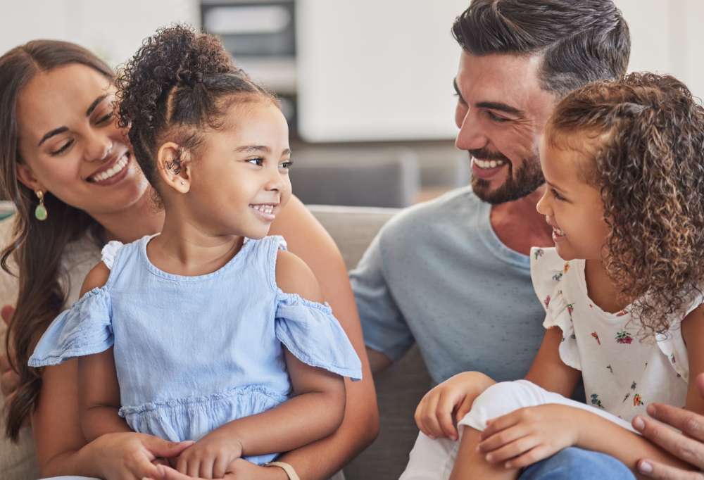 a family of four, a man and a woman with little girls sitting on their knees