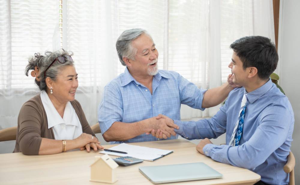 An cheerful elderly couple shake the hand of a solicitor after resolving a will dispute