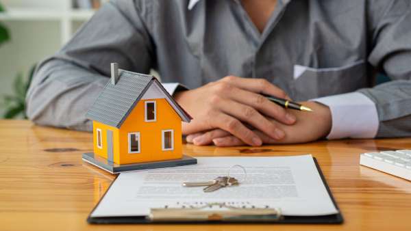 A small model of a house and house keys lay upon a contract