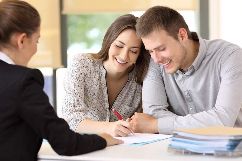 A cheerful young couple sign a document during a lasting power of attorney consultation