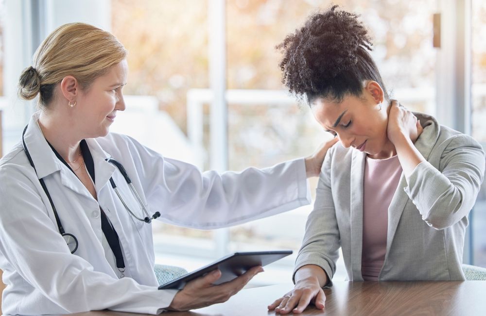 Personal Injury A patient winces and holds her injured neck during an appointment with her doctor