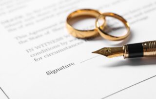 a prenuptial agreement document with two different sized gold wedding rings and a gold tip pen